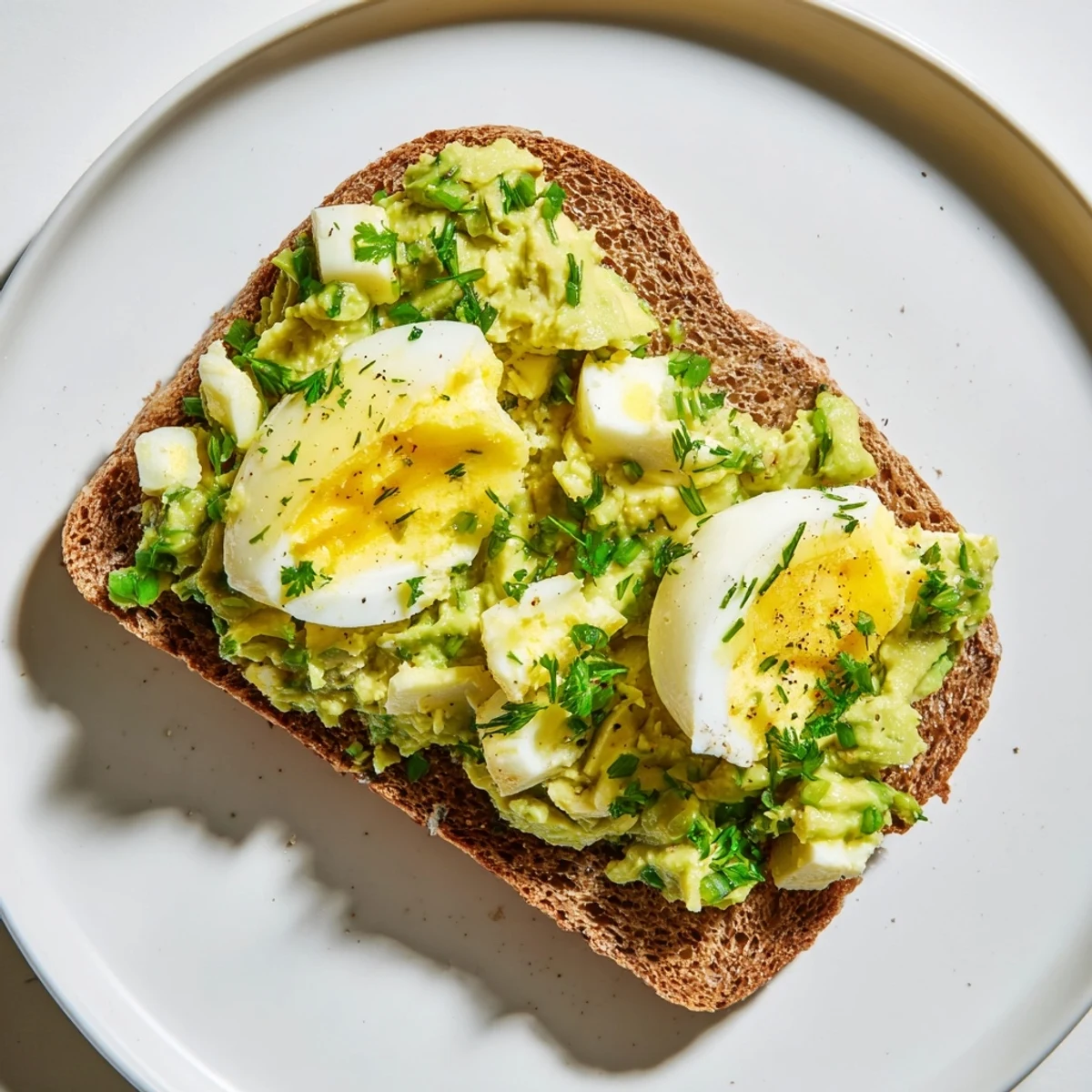 Close-up of fluffy Avocado Egg Smash spread on toast, garnished with fresh chives, ready to eat.