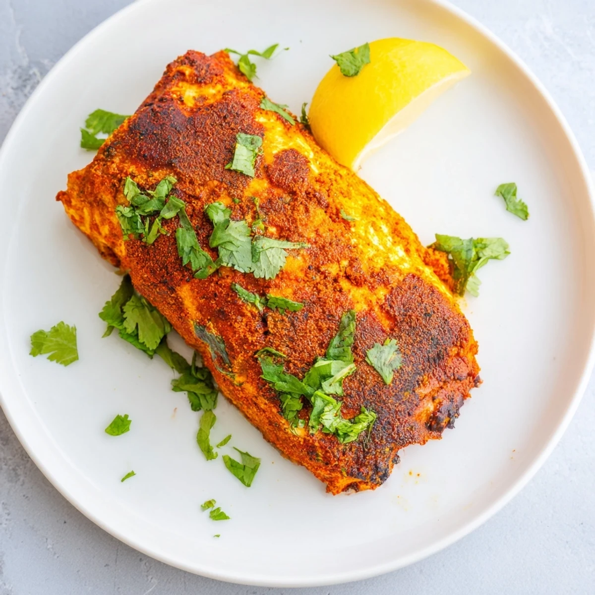 Close-up of golden-brown Indian Tikka Salmon, garnished with fresh cilantro and lemon wedges.
