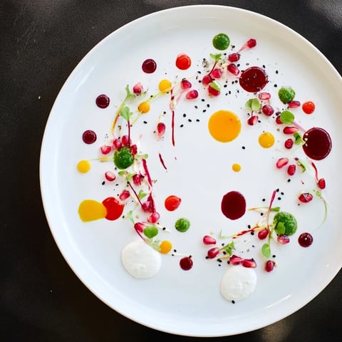 A plate showcases the Pointillism Dot Matrix, a vibrant vegetarian appetizer with colorful vegetable purees.