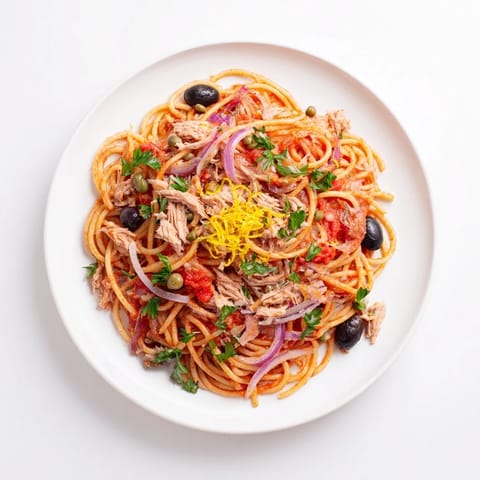 Close-up photo of pasta with tuna, olives, and capers, boasting colorful Mediterranean flavors.