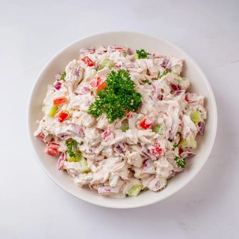 A close-up of delicious canned chicken salad speckled with herbs, ready to serve.