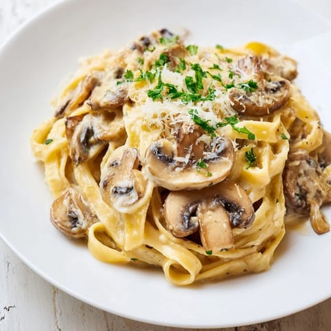 A close-up of creamy mushroom Alfredo, the fettuccine noodles twirling with golden, sautéed mushrooms and fresh parsley.