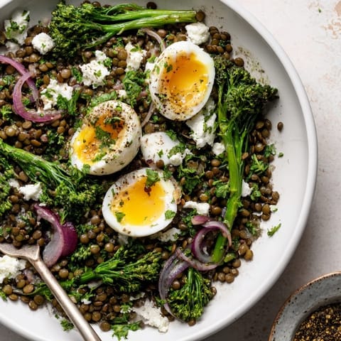 Steaming French lentil salad topped with bright green broccolini, fresh parsley, and creamy soft-cooked eggs, finished with crumbled goat cheese and black pepper.