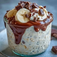 A jar of creamy overnight oats layered with fresh banana slices and rich dark chocolate chunks.  